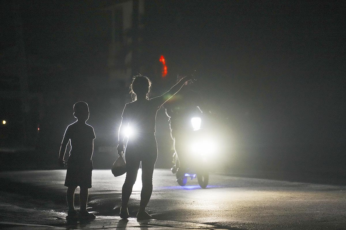 En pojke och en kvinna liftar i mörkret under ett av många planerade elavbrott i energikrisens Kuba. Foto: AP/TT